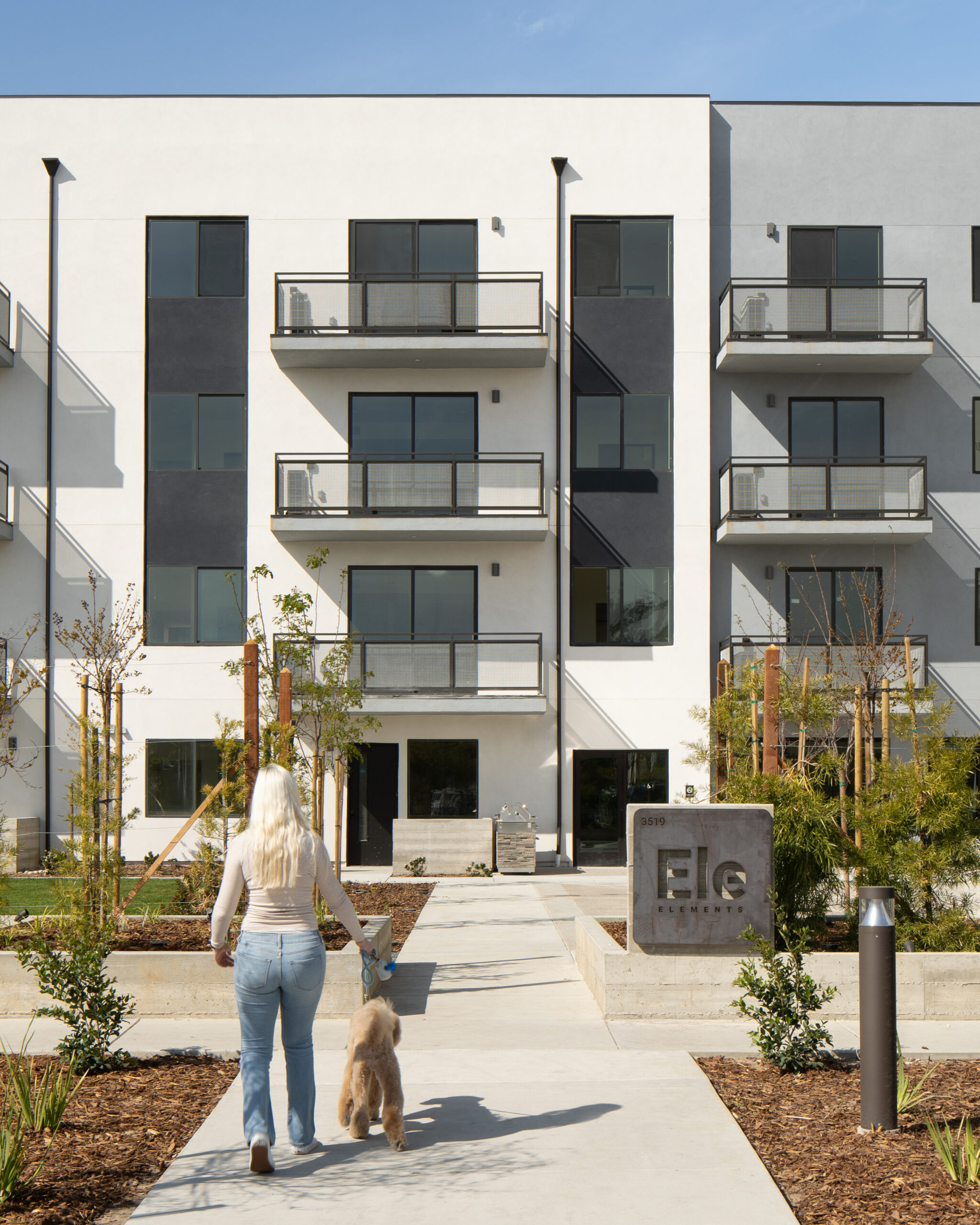 Architectural photograph of model and dog walking into main facade of Elements Apartments during the daytime